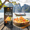 SIAM Noodles Kit Pad Thai with a scenic background of mountains and water.
