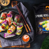 Colorful spring rolls on a plate with dipping sauces and chopsticks, next to a SIAM branded package.