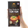 Hand holding a Siam brand Tom Yum soup noodles kit packaging.