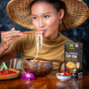 Woman eating noodles with a 'Tom Yum' soup kit on a table