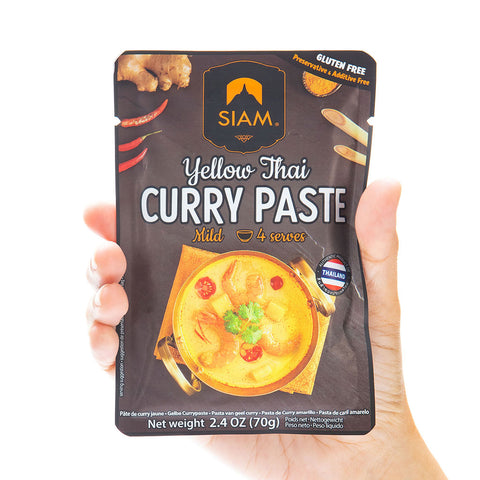 Hand holding a package of Siam Yellow Thai Curry Paste on a white background